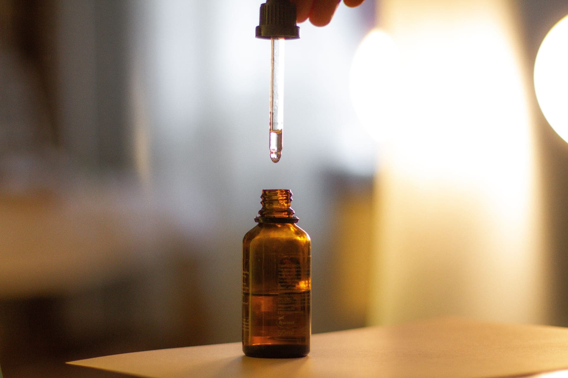 An amber glass serum dropper resting on a warm stone surface in low evening light